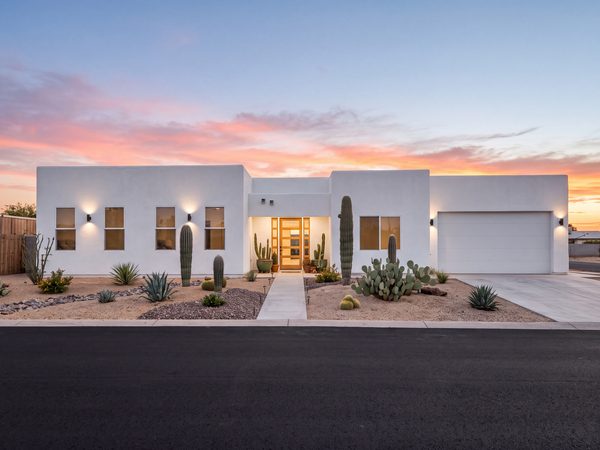 White stucco single-story Arizona home with wood front door and desert landscaping at sunset
